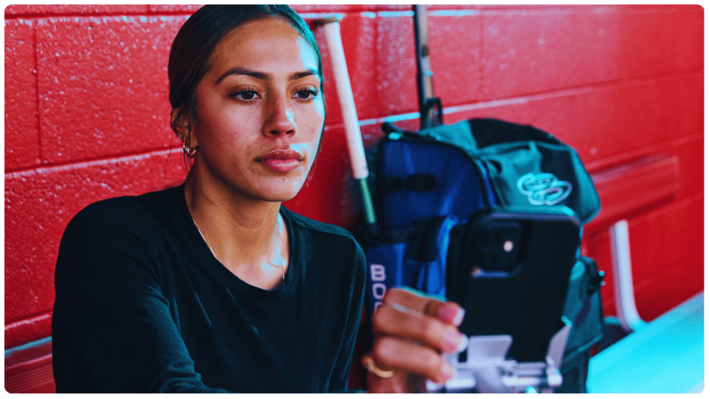 Female athlete using an AI baseball coach app on her smartphone in the dugout for training tips and game-day mental prep